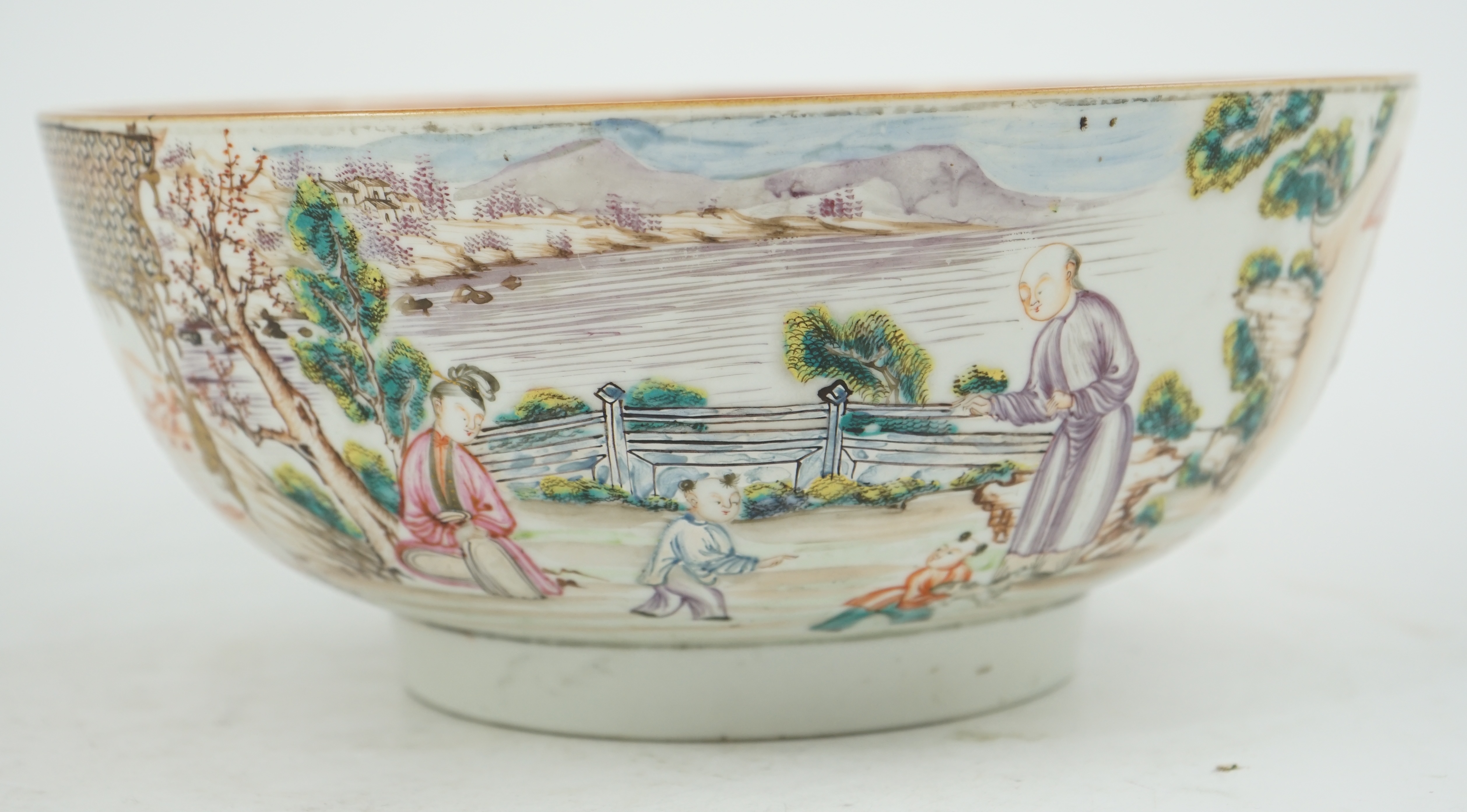 A Chinese famille rose ‘mandarin’ bowl, Qianlong period, painted with figures in a lakeside garden, between red enamelled landscape vignettes and cellular panels, 28.4cm diameter. Condition - there is a hairline crack to